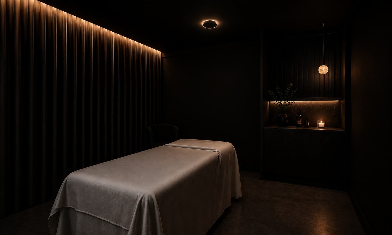 A draped massage table beside a candlelit stone alcove in the low-lit treatment room at Composure Club